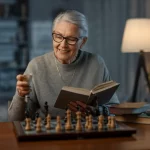 Immagine fotorealistica di una donna anziana sorridente e attiva (sui 70 anni) che gioca a scacchi o legge un libro, simboleggiando la salute cognitiva in età avanzata. Obiettivo prime 50mm, luce calda e naturale, profondità di campo per mettere a fuoco lei e sfocare leggermente lo sfondo.