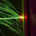 Fotografia macro di microparticelle sospese in un liquido trasparente all'interno di un dispositivo microfluidico, illuminate da un raggio laser focalizzato che crea un punto caldo visibile, con scie di flusso stilizzate che indicano il movimento. Obiettivo macro 100mm, alta definizione, illuminazione controllata, profondità di campo ridotta.