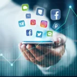Immagine concettuale che mostra una mano che tiene uno smartphone con icone di social media luminose fluttuanti, sovrapposta a una grafica astratta e dinamica che rappresenta grafici stilizzati di engagement e soddisfazione lavorativa in crescita, ambientata in un contesto aziendale moderno e sfocato. Illuminazione drammatica high-key, obiettivo macro 100mm per dettaglio estremo sulle icone e sulla mano, colori vivaci ma professionali (blu, verde, bianco).