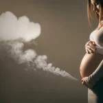 Immagine simbolica: una donna incinta protegge amorevolmente il suo pancione, sfondo leggermente sfocato con una nuvola stilizzata di fumo in lontananza che si dissolve, luce calda e protettiva, obiettivo 50mm, profondità di campo.