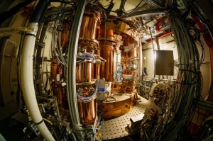 Immagine fotorealistica dell'interno high-tech di un esperimento di fisica dei neutrini (CONUS+) vicino a un reattore nucleare, con rivelatori al germanio circondati da uno scudo complesso di piombo e polietilene, illuminazione drammatica, obiettivo prime 35mm, profondità di campo, che evoca la ricerca scientifica e la sfida del rumore di fondo.