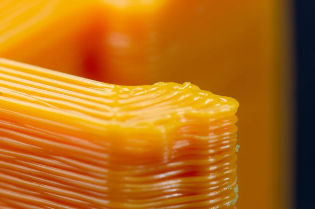 Immagine macro fotorealistica di un pezzo complesso stampato in 3D con filamento PLA colorato, che mostra la texture superficiale e la stratificazione, obiettivo macro 105mm, illuminazione da studio controllata per massima definizione, messa a fuoco selettiva sulla parte anteriore dell'oggetto.