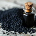 Fotografia macro di semi neri di Nigella Sativa sparsi su una superficie di legno rustico, accanto a una piccola ampolla di vetro contenente olio di cumino nero dal colore ambrato scuro. Luce laterale morbida che evidenzia la texture dei semi e la viscosità dell'olio. Lente macro 100mm, alta definizione, messa a fuoco precisa sui semi in primo piano.