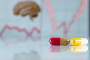 Primo piano di capsule di Trimetazidina e Olanzapina affiancate su una superficie riflettente da laboratorio, con sfondo sfocato di grafici stilizzati rappresentanti l'attività cerebrale e muscolare. Obiettivo macro 100mm, alta definizione, illuminazione controllata e precisa che crea riflessi morbidi.