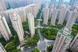 Veduta aerea, scattata con un obiettivo grandangolare (es. 24mm), di un quartiere residenziale densamente popolato in una città cinese, dove spiccano ampie aree verdi ben curate (parchi, giardini condominiali) tra gli edifici. Luce diurna chiara, alta definizione per mostrare il contrasto tra costruito e natura.