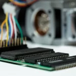 Immagine macro di un circuito elettronico con un chip DSP in primo piano, collegato a fili colorati che portano a un motore elettrico sfocato sullo sfondo, macro lens 100mm, high detail, precise focusing, illuminazione da laboratorio controllata, simboleggia il controllo avanzato dei motori.