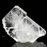 Macro fotografia, obiettivo 60mm, di un cristallo singolo trasparente e incolore di TMCM-CdCl3 che mostra sfaccettature intricate, appoggiato su una superficie scura con riflessi sottili, illuminazione controllata che ne evidenzia la struttura cristallina, alto dettaglio, messa a fuoco precisa.