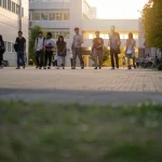 Immagine fotorealistica di un campus universitario giapponese moderno e diversificato al tramonto, con studenti di varie etnie che interagiscono pacificamente. Obiettivo grandangolare 24mm, luce calda e accogliente, messa a fuoco nitida.