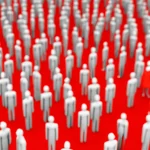 Fotografia concettuale, obiettivo 35mm, bianco e nero con un elemento di colore rosso acceso, profondità di campo. Una folla omogenea e grigia (mainstream) da cui emerge una singola figura o un flusso rosso (radicale) che inizia a diffondersi, simboleggiando il concetto di mainstream radicalizzato.