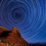 Fotografia paesaggistica grandangolare di una complessa rete di canyon illuminati dalla luce stellare, lunga esposizione per catturare il movimento delle stelle come archi luminosi che collegano diverse parti del paesaggio, obiettivo grandangolare 15mm, messa a fuoco nitida.