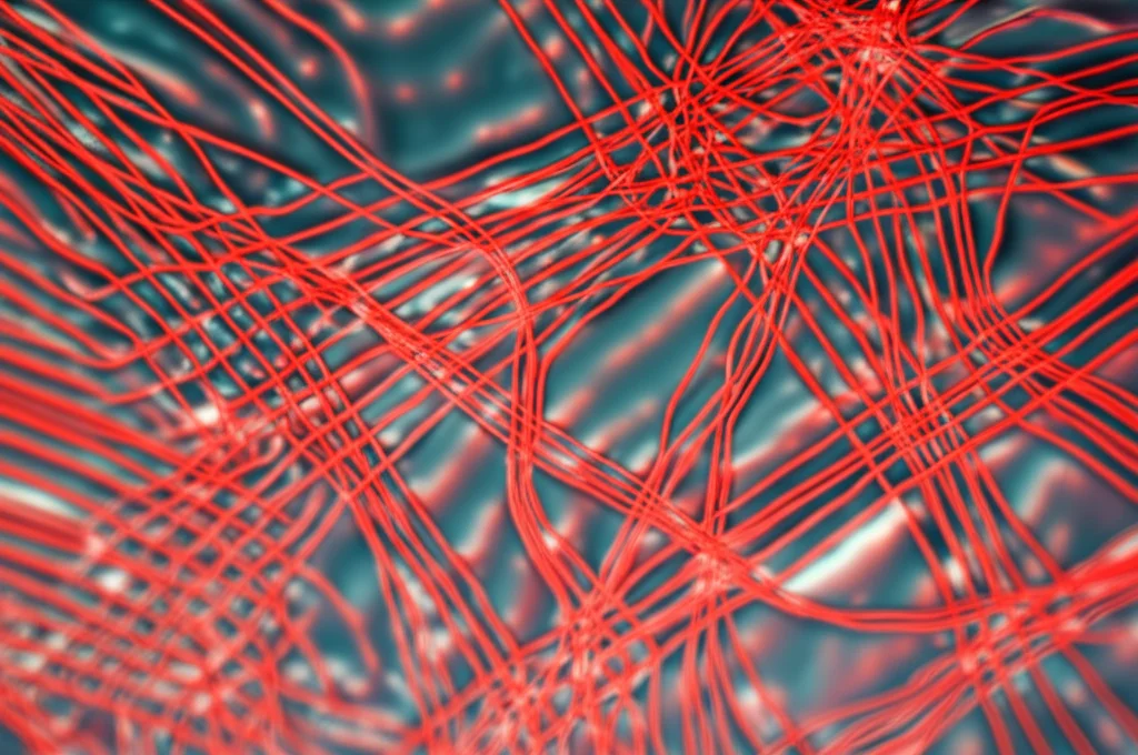 Primo piano fotorealistico di nanoparticelle di ferrite Co-Mn-Cr sospese in un fluido trasparente, che mostrano deboli emissioni rosse e interazioni con un campo magnetico esterno visibile come linee di forza sfocate, obiettivo macro 90mm, illuminazione laterale controllata, alta definizione, messa a fuoco precisa.