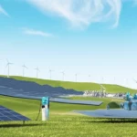Immagine panoramica di un paesaggio energetico integrato e sostenibile: turbine eoliche su colline verdi, pannelli solari che coprono campi e tetti, una diga idroelettrica moderna, una centrale mareomotrice stilizzata visibile sulla costa e diverse auto elettriche collegate a stazioni di ricarica intelligenti in un contesto urbano/suburbano pulito. Wide-angle lens, 10mm, sharp focus, luce solare brillante e chiara, cielo azzurro con poche nuvole bianche.