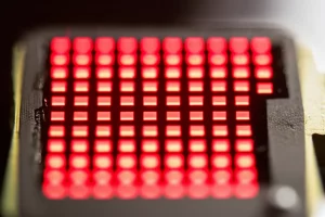 Fotografia macro di un prototipo di display QLED tandem face-to-face acceso, che mostra pixel rossi brillanti ad altissima efficienza, obiettivo macro 90mm, illuminazione da studio controllata, focus nitido sulla struttura stratificata del dispositivo, sfondo high-tech sfocato.