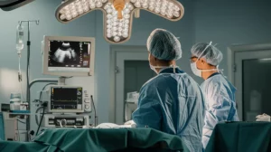 Immagine fotorealistica di una sala operatoria moderna durante un intervento di tiroidectomia. Si vede il team chirurgico concentrato sul paziente, monitor con immagini ecografiche e tracciati di neuromonitoraggio visibili sullo sfondo. Luce chirurgica intensa illumina il campo operatorio. 35mm prime lens, profondità di campo che mette a fuoco il chirurgo principale.
