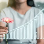 Primo piano di una donna dall'aspetto sano che tiene delicatamente un fiore stilizzato che si trasforma in un grafico di dati sanitari ascendente, simboleggiando la salute riproduttiva e la ricerca. Luce morbida, sfondo leggermente sfocato. Obiettivo prime, 50mm, profondità di campo.