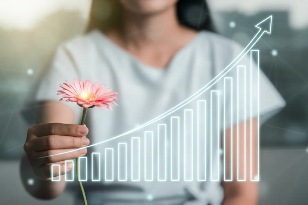 Primo piano di una donna dall'aspetto sano che tiene delicatamente un fiore stilizzato che si trasforma in un grafico di dati sanitari ascendente, simboleggiando la salute riproduttiva e la ricerca. Luce morbida, sfondo leggermente sfocato. Obiettivo prime, 50mm, profondità di campo.