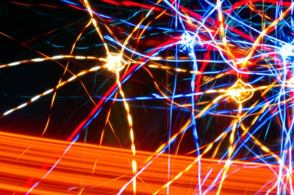 Rappresentazione astratta della comunicazione neuro-immunitaria, con percorsi neurali luminosi intrecciati a forme stilizzate di cellule immunitarie, effetto lunga esposizione sulle parti luminose, obiettivo grandangolare 20mm, messa a fuoco nitida.