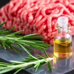 Composizione still life con rametti di rosmarino fresco, una boccetta di olio essenziale, un campione trasparente di film multistrato a base di chitosano e carne macinata fresca sullo sfondo, obiettivo macro 90mm, alta definizione, illuminazione naturale controllata, focus preciso sui dettagli del film e del rosmarino.