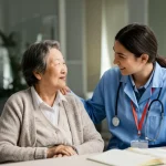 Fotografia realistica toccante di un'anziana signora cinese che sorride calorosamente mentre interagisce con un'operatrice sanitaria o un volontario più giovane in un ambiente ospedaliero luminoso e accogliente. Obiettivo prime 50mm, profondità di campo che isola i due soggetti, luce calda e naturale, focus sull'interazione umana e sul supporto sociale.