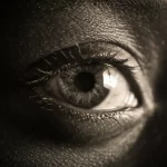 Primo piano drammatico dell'occhio di un bambino africano che riflette una zanzara Anopheles, simbolo della malaria; fotografia ritrattistica con lente prime 35mm, duotone seppia e grigio scuro, profondità di campo marcata.