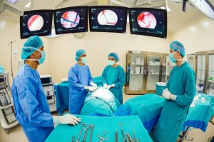 Fotografia dettagliata di una sala operatoria high-tech durante un intervento di chirurgia rettale mininvasiva, con monitor che mostrano immagini endoscopiche e un team chirurgico concentrato, obiettivo grandangolare 24mm, illuminazione chirurgica brillante, messa a fuoco nitida sull'azione centrale.