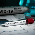 Immagine fotorealistica di una provetta etichettata 'Hydroxychloroquine' posta su un tavolo da laboratorio accanto a grafici scientifici e ritagli di giornale con titoli sulla pandemia COVID-19. Illuminazione drammatica stile film noir, profondità di campo ridotta, obiettivo 35mm, per simboleggiare la controversia e l'urgenza della ricerca scientifica durante una crisi sanitaria.