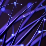Primo piano macro estremo di sottili aghi in fibra di carbonio, simili a setole di un pennello, da cui emanano scintille luminose blu e viola (rappresentazione degli ioni positivi e negativi). Lo sfondo è scuro e leggermente sfocato per mettere in risalto gli aghi. Illuminazione controllata e drammatica che evidenzia i dettagli delle fibre e l'emissione ionica. Obiettivo macro 100mm, alta definizione, messa a fuoco precisa sugli aghi.