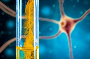 Primo piano macro di polvere di curcuma dorata brillante che si dissolve delicatamente in acqua chiara all'interno di una provetta da laboratorio, con una rappresentazione stilizzata di un neurone sano sullo sfondo sfocato. Lente macro 100mm, alta definizione, illuminazione da studio controllata per creare riflessi sull'acqua e sulla polvere, messa a fuoco precisa sulla curcumina in dissoluzione.