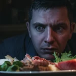 Una persona guarda con sospetto e disgusto un piatto contenente cibi esotici e sconosciuti, illuminazione drammatica laterale che accentua l'espressione facciale, obiettivo 50mm, profondità di campo che sfoca leggermente lo sfondo, stile realistico ad alto dettaglio.