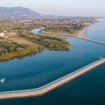 Veduta aerea della costa campana dove un fiume incontra il mare, mostrando la transizione tra terreni agricoli, aree urbanizzate e l'acqua, lente grandangolare 20mm, lunga esposizione per acqua liscia, luce del mattino.