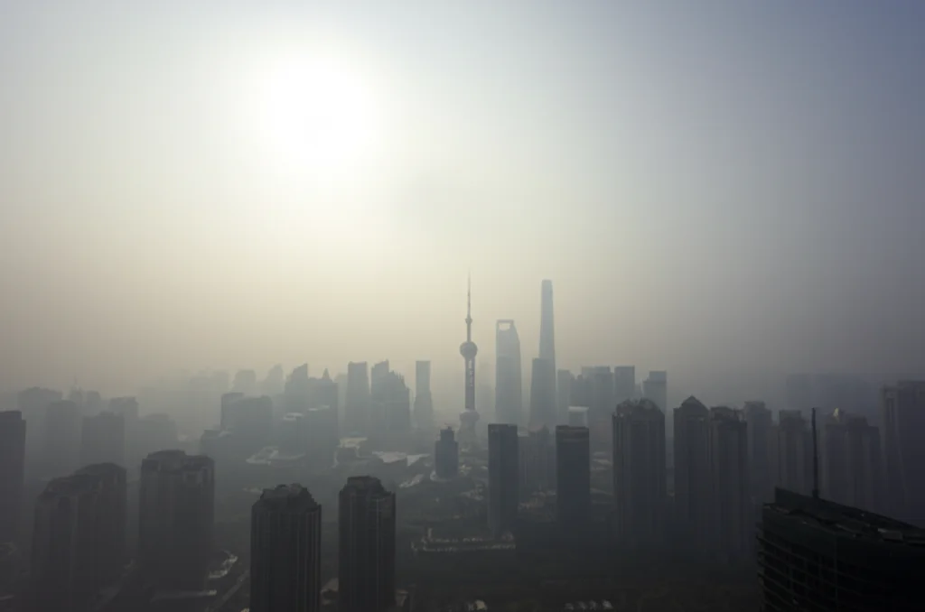 Fotografia grandangolare 10mm di uno skyline di una metropoli cinese avvolto in una densa foschia di inquinamento PM2.5, con edifici iconici appena visibili, luce diffusa e piatta, messa a fuoco nitida sull'intera scena.