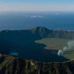 Veduta aerea ampia dei Campi Flegrei che mostra la caldera, il mare e l'area urbanizzata circostante, con leggere fumarole visibili dalla Solfatara. Landscape wide angle 15mm, sharp focus, luce del mattino, atmosfera vibrante.
