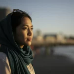 Immagine fotorealistica di una donna indonesiana adulta che guarda con fiducia verso l'orizzonte, simboleggiando scelta e futuro, ambientazione esterna luminosa al tramonto, obiettivo 50mm, profondità di campo che sfoca leggermente lo sfondo, luce calda.