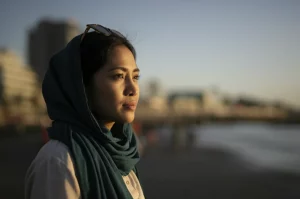 Immagine fotorealistica di una donna indonesiana adulta che guarda con fiducia verso l'orizzonte, simboleggiando scelta e futuro, ambientazione esterna luminosa al tramonto, obiettivo 50mm, profondità di campo che sfoca leggermente lo sfondo, luce calda.