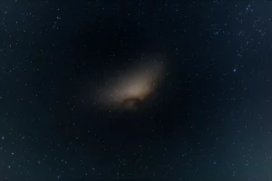 Fotografia astronomica grandangolare, 10mm, lunga esposizione, della Via Lattea vista dalla Terra, con una debole ma estesa nube oscura a forma di mezzaluna (Eos) evidenziata in una regione del cielo vicino allo Sperone Polare Nord, messa a fuoco nitida, cielo notturno profondo.