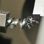 Fotografia macro ad alta definizione di un truciolo metallico che si stacca da un pezzo in lavorazione su un tornio. L'angolo di flusso del truciolo è chiaramente visibile. Illuminazione controllata, obiettivo macro 90mm, messa a fuoco selettiva sul punto di taglio.