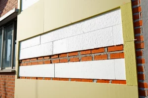 Immagine fotorealistica di una sezione trasversale di un muro esterno di una casa rurale cinese durante una ristrutturazione energetica. Si vedono i mattoni originali, uno strato spesso di pannelli isolanti (EPS) applicati esternamente, e la nuova finitura. Obiettivo 50mm, luce da cantiere che evidenzia i diversi strati, alta definizione dei materiali, focus sui dettagli tecnici della ristrutturazione.