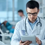 Medico che esamina attentamente i risultati di un esame del sangue su un tablet in un ambiente ospedaliero luminoso, lente prime 50mm, profondità di campo che sfoca leggermente lo sfondo, focus sui dati e sull'espressione concentrata del medico.