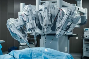 Immagine fotorealistica di una sala operatoria focalizzata sui bracci di un robot chirurgico posizionati con precisione sopra un paziente (fuori fuoco). Illuminazione soffusa e sterile, leggera profondità di campo. Obiettivo prime, 35mm.