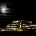 Immagine notturna suggestiva della luna piena che splende sopra il profilo di un pronto soccorso ospedaliero moderno. Fotografia astronomica, obiettivo grandangolare 15mm, lunga esposizione per enfatizzare la luce lunare, focus nitido.