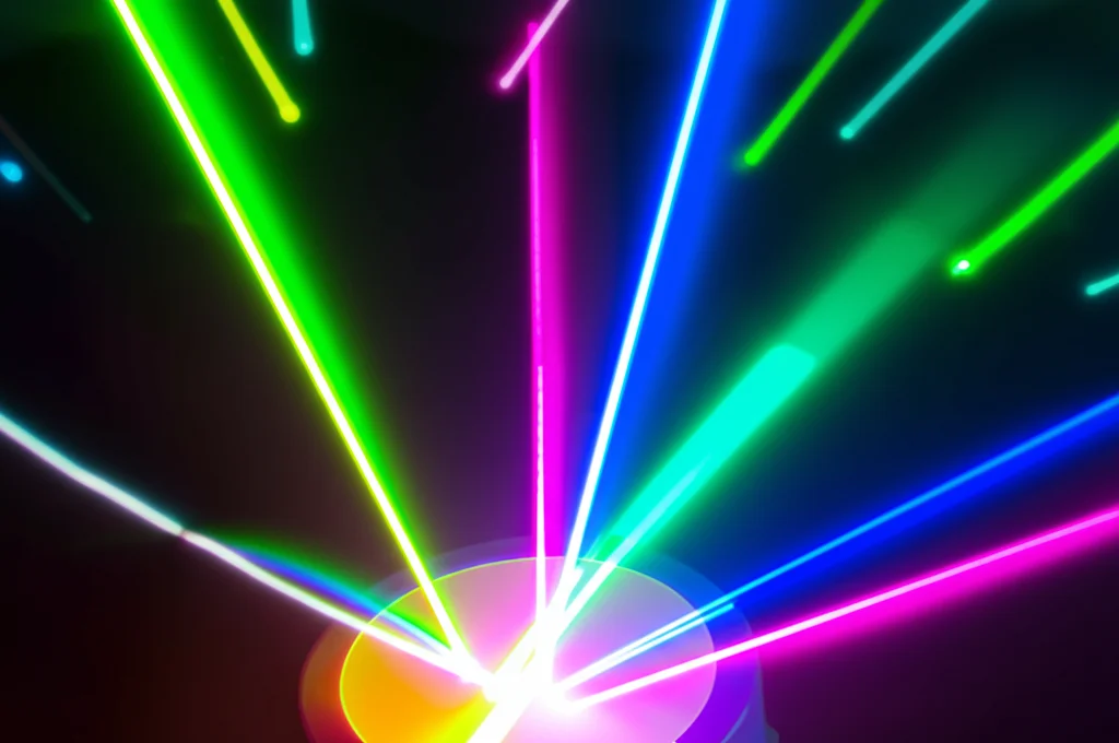 Visualizzazione artistica e fotorealistica di un fascio laser complesso che viene modellato da una metasuperficie compatta. Si vedono diversi fasci colorati emergere, rappresentanti i molteplici gradi di libertà controllati (vettore d'onda, fase, OAM, SAM, ampiezza, modo spaziale). Lente prime 35mm, profondità di campo, colori vibranti su sfondo scuro high-tech.