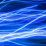 Visualizzazione astratta di impulsi di energia elettromagnetica che fluiscono velocemente attraverso una rete complessa di nodi interconnessi, simboleggiando l'accelerazione della simulazione. Effetto motion blur leggero, colori vibranti blu ed elettrico, teleobiettivo zoom 100mm, fast shutter speed.