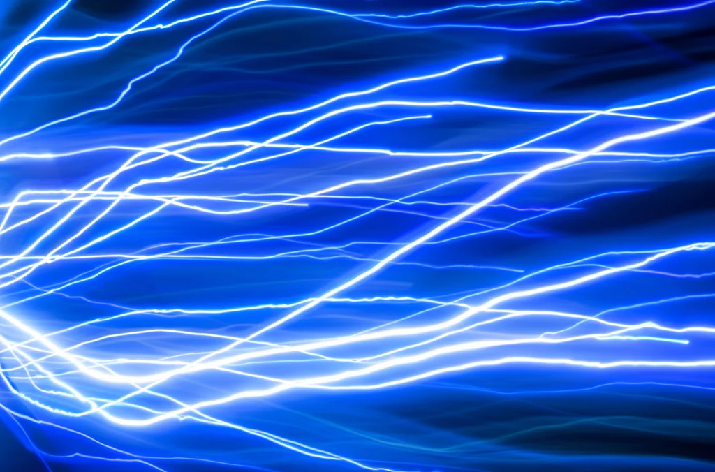Visualizzazione astratta di impulsi di energia elettromagnetica che fluiscono velocemente attraverso una rete complessa di nodi interconnessi, simboleggiando l'accelerazione della simulazione. Effetto motion blur leggero, colori vibranti blu ed elettrico, teleobiettivo zoom 100mm, fast shutter speed.