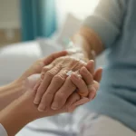Fotografia simbolica: una mano anziana e fragile tenuta con cura da una mano più giovane con guanto medico in un ambiente ospedaliero luminoso ma intimo, prime lens 35mm, depth of field, toni caldi, rappresenta la compassione e il supporto nelle cure palliative generali.