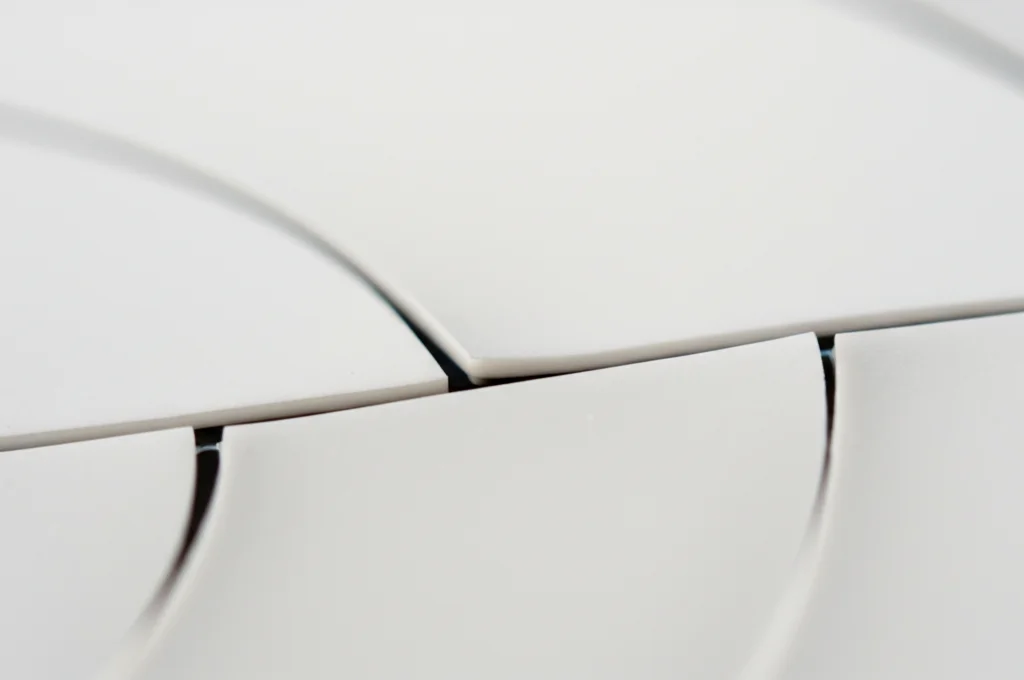 Primo piano macro di una crepa sottile che si allarga su una superficie di porcellana bianca. Illuminazione controllata e precisa che evidenzia la fragilità e la tensione. Obiettivo macro 100mm, alta definizione, messa a fuoco selettiva sulla crepa.