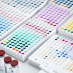 Fotografia macro, obiettivo 90mm, di piastre microtiter ELISA con pozzetti colorati che indicano risultati, affiancate a cassette di test rapidi e fiale, suggerendo un confronto tra test anticorpali SARS-CoV-2. Illuminazione controllata, alto dettaglio.