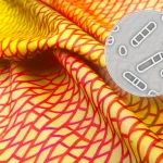 Immagine fotorealistica, obiettivo 35mm con profondità di campo, che mostra rotoli di tessuto di poliestere dai colori vivaci (giallo, rosso, marrone) stampati con motivi geometrici sottili. Sovrapposta in modo discreto su una parte del tessuto, si intravede una grafica stilizzata che rappresenta una zona di inibizione batterica, suggerendo la doppia funzionalità estetica e antibatterica del materiale.
