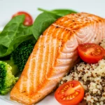 Primo piano di un piatto colorato e salutare simbolo di una dieta anti-infiammatoria: salmone grigliato adagiato su un letto di quinoa, accompagnato da broccoli al vapore, pomodorini ciliegino tagliati a metà e qualche foglia di spinacio fresco. Macro lens, 100mm, high detail, precise focusing sul salmone e le verdure, controlled lighting dall'alto leggermente laterale per creare ombre morbide, sfondo neutro sfocato.