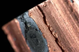 Primo piano fotorealistico, obiettivo macro (90mm), che mostra gli strati distinti di un campione di composito metallico ferro-rame dopo un test balistico. Focus sull'interfaccia tra lo strato rossastro di rame e il nucleo di ferro più scuro, mostrando deformazione e texture. Alto dettaglio, illuminazione controllata.