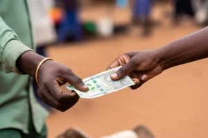Immagine fotorealistica che cattura l'essenza delle scelte di consumo sostenibile in Zimbabwe. Una mano porge una banconota locale per acquistare un prodotto con etichetta ecologica ben visibile da un venditore sorridente in un mercato all'aperto. Macro lens 85mm, high detail sul prodotto e sulle mani, sfondo leggermente sfocato per enfatizzare l'interazione e la scelta consapevole.